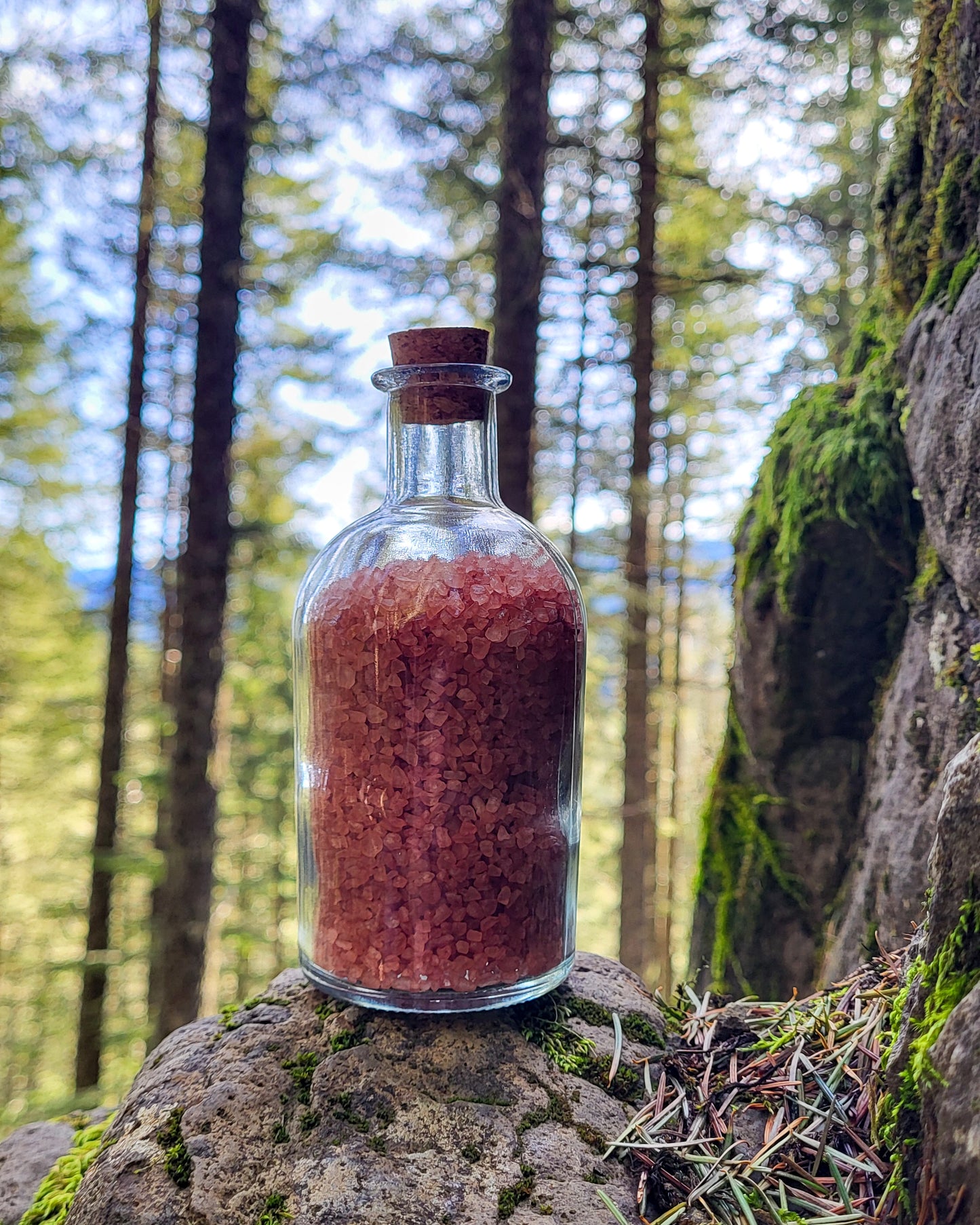 Rainier natural bath salts warm cinnamon scent in corked glass bottle displayed against a mountain overlook backdrop