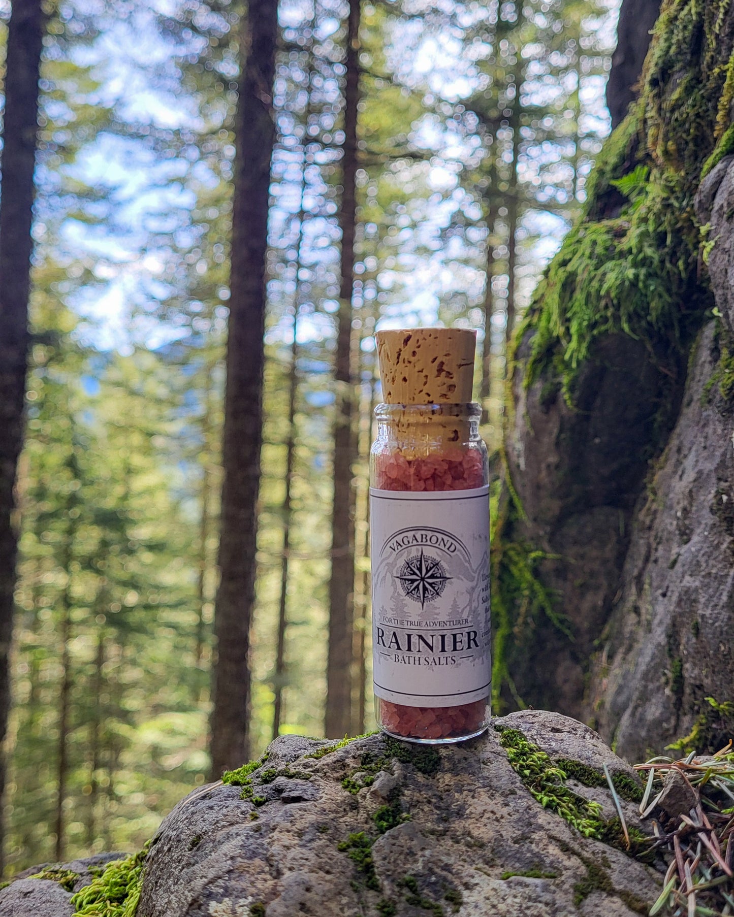 Rainier natural bath salts warm cinnamon scent in corked glass bottle displayed against a mountainside backdrop