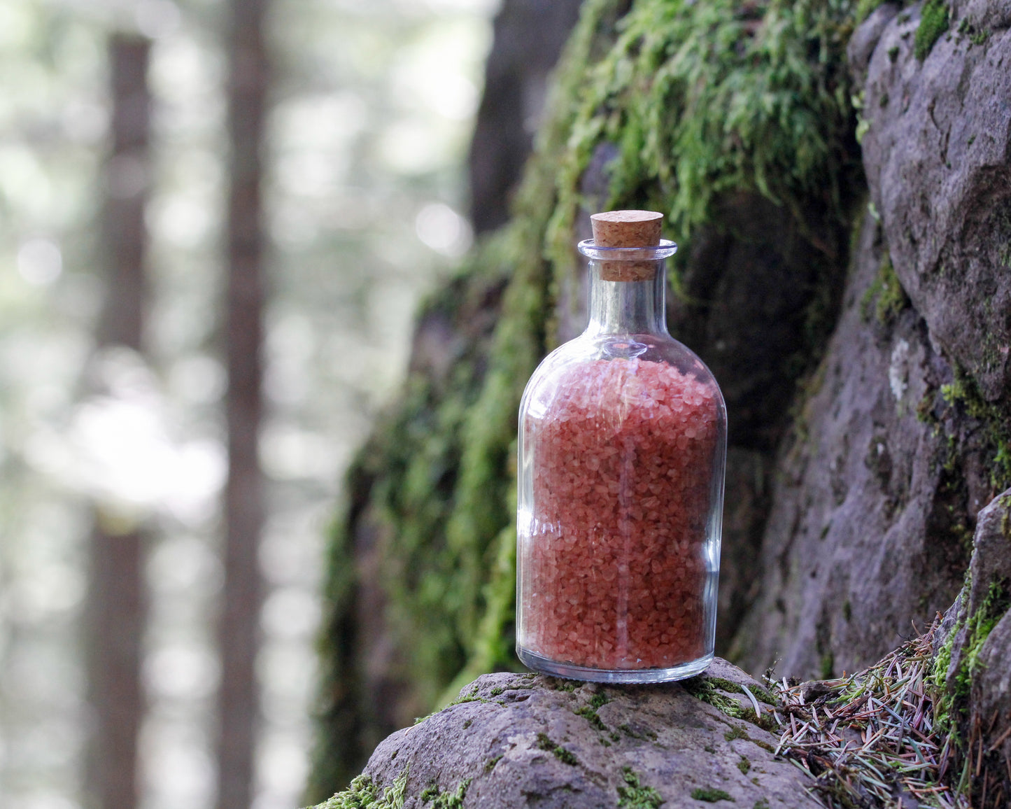 Rainier natural bath salts warm cinnamon scent in corked glass bottle displayed against a mountainside backdrop