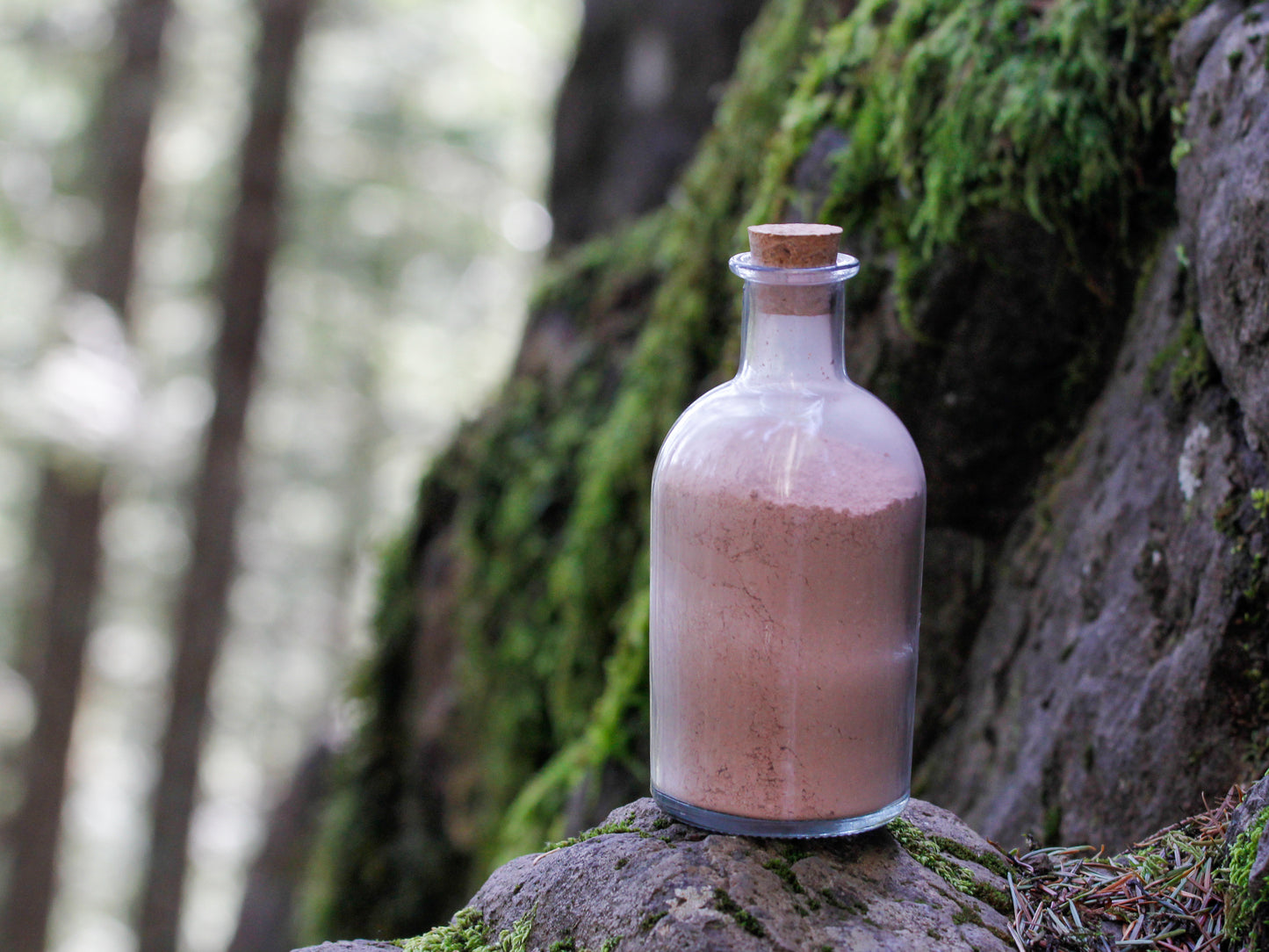 Rainier natural clay mask in corked glass bottles displayed against a mountainside backdrop.
