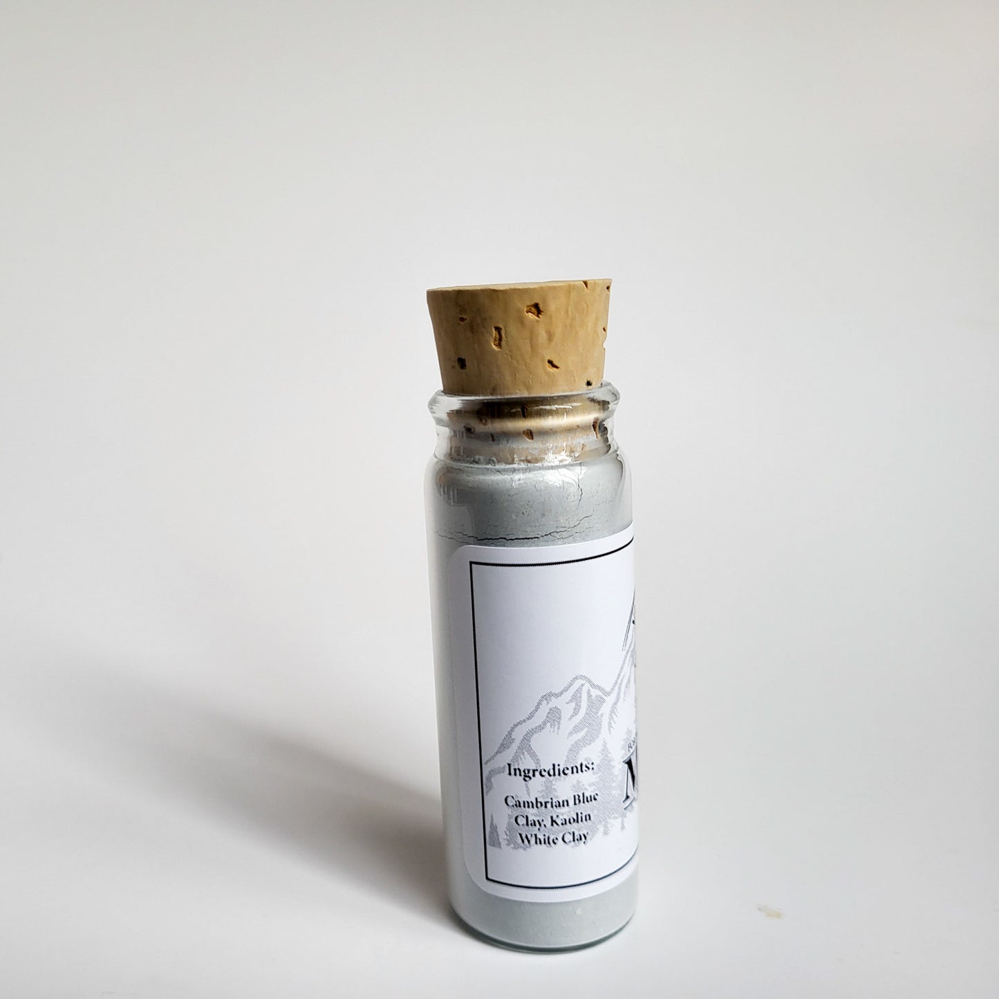 Muir natural clay mask in corked glass bottle displayed against a plain white backdrop showing ingredients on the label