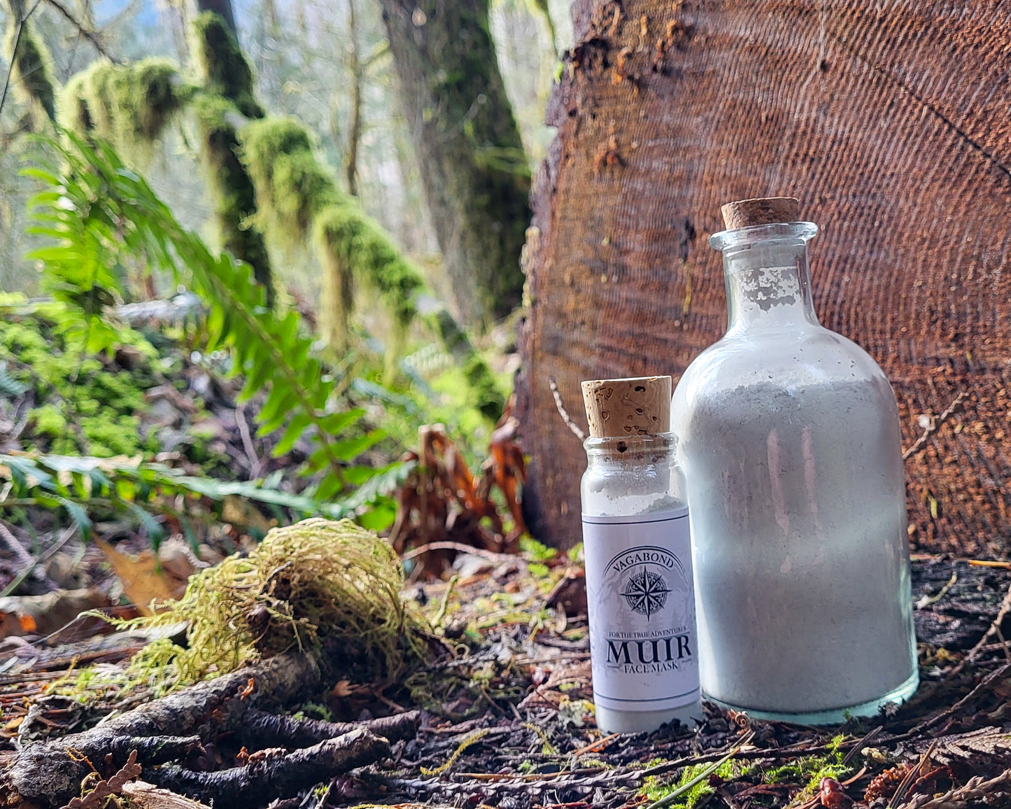 Muir natural clay mask in corked glass bottles displayed on a split log backdrop.