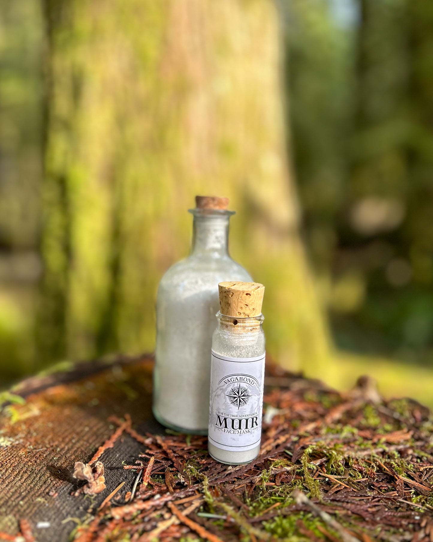 Muir natural clay mask in corked glass bottles displayed on a forest stump backdrop.