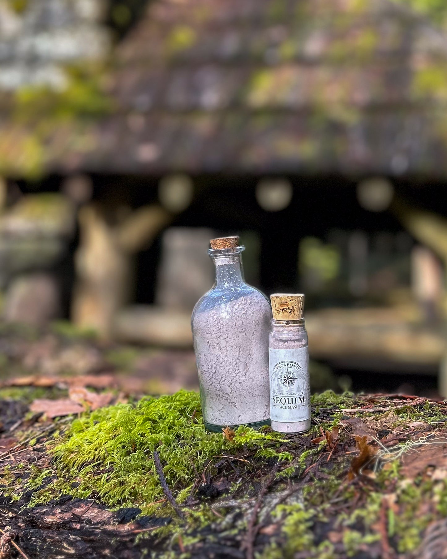 Sequim natural clay mask in corked glass bottles displayed against a blurry cabin backdrop.