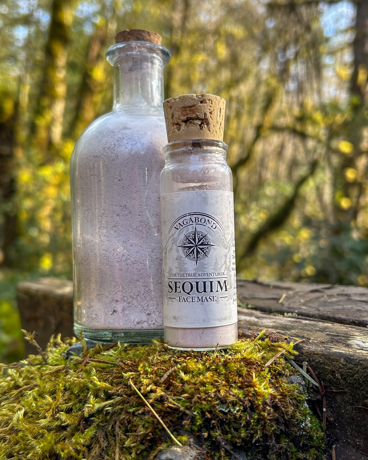Sequim natural clay mask in corked glass bottles displayed against a blurry forest backdrop.