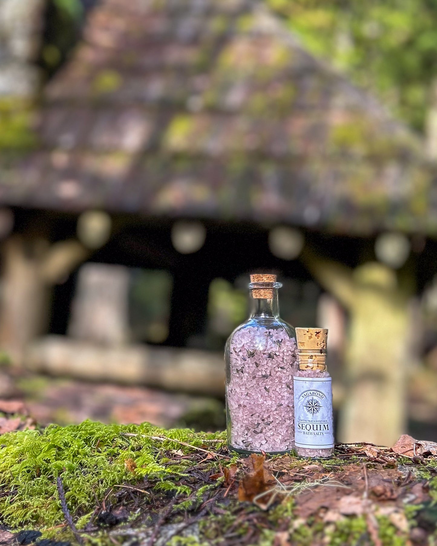 Sequim natural bath salts lavender mint scent in corked glass bottle displayed against a mossy cabin backdrop