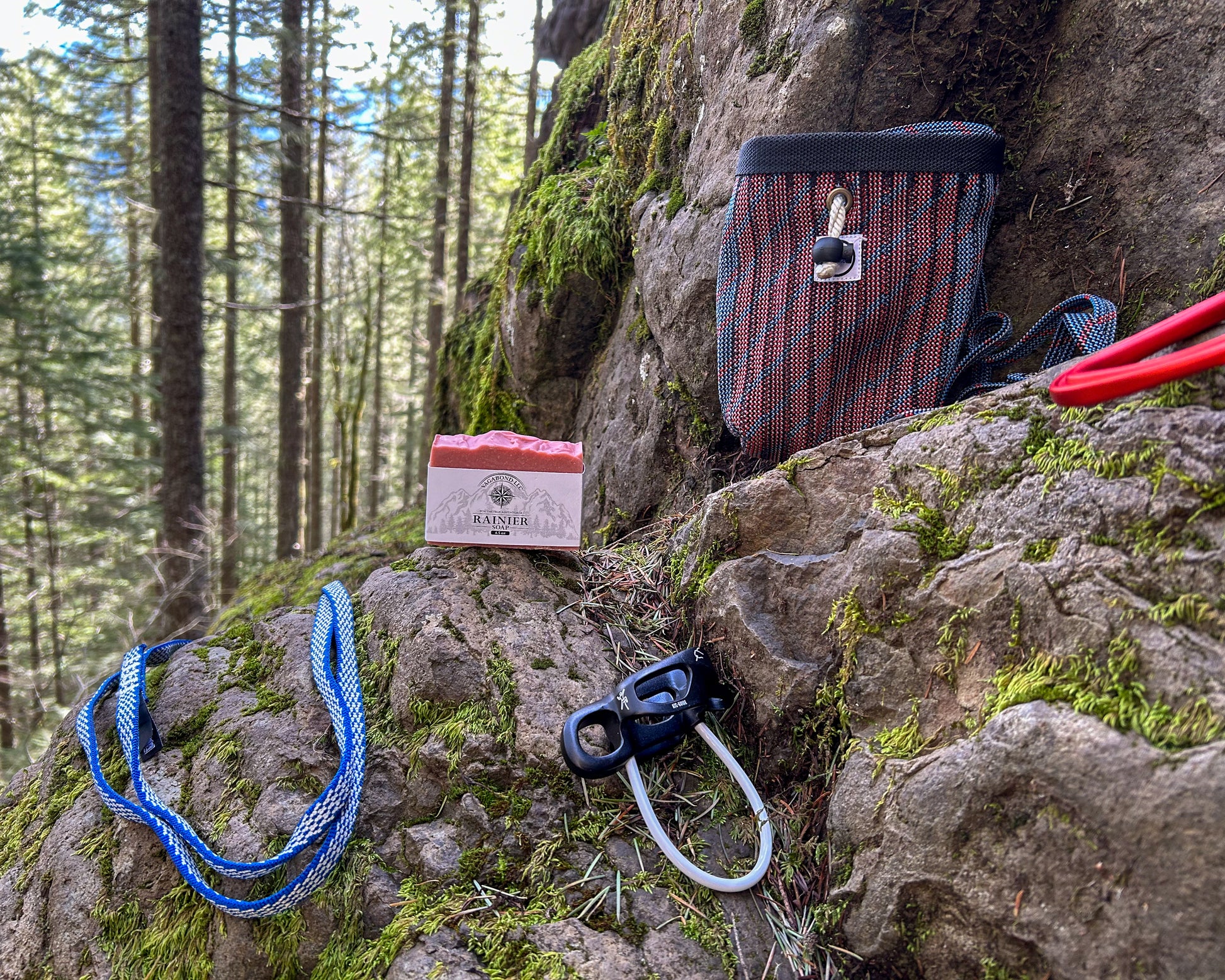 Rainier natural bar soap warm cinnamon scent on a log displayed with climbing gear against a mountainside backdrop.