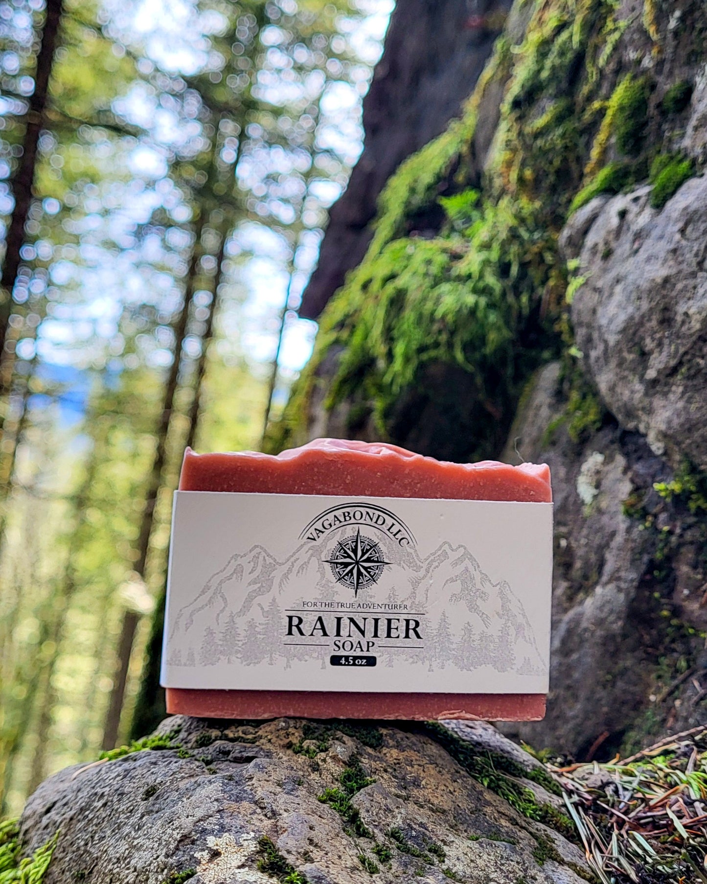 Rainier natural bar soap warm cinnamon scent on a log displayed against a mountainside backdrop.