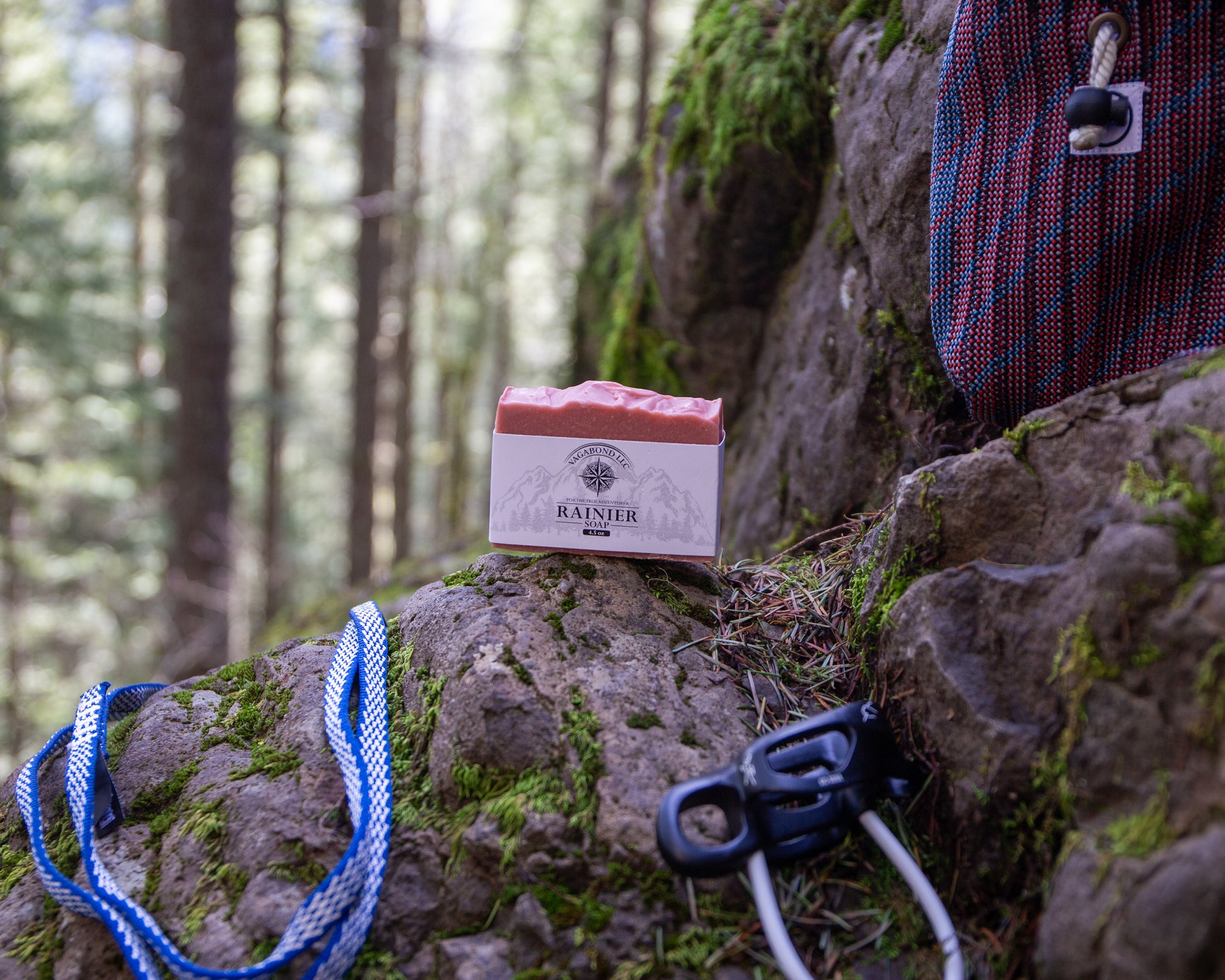 Rainier natural bar soap warm cinnamon scent on a log displayed with climbing gear against a mountainside backdrop.