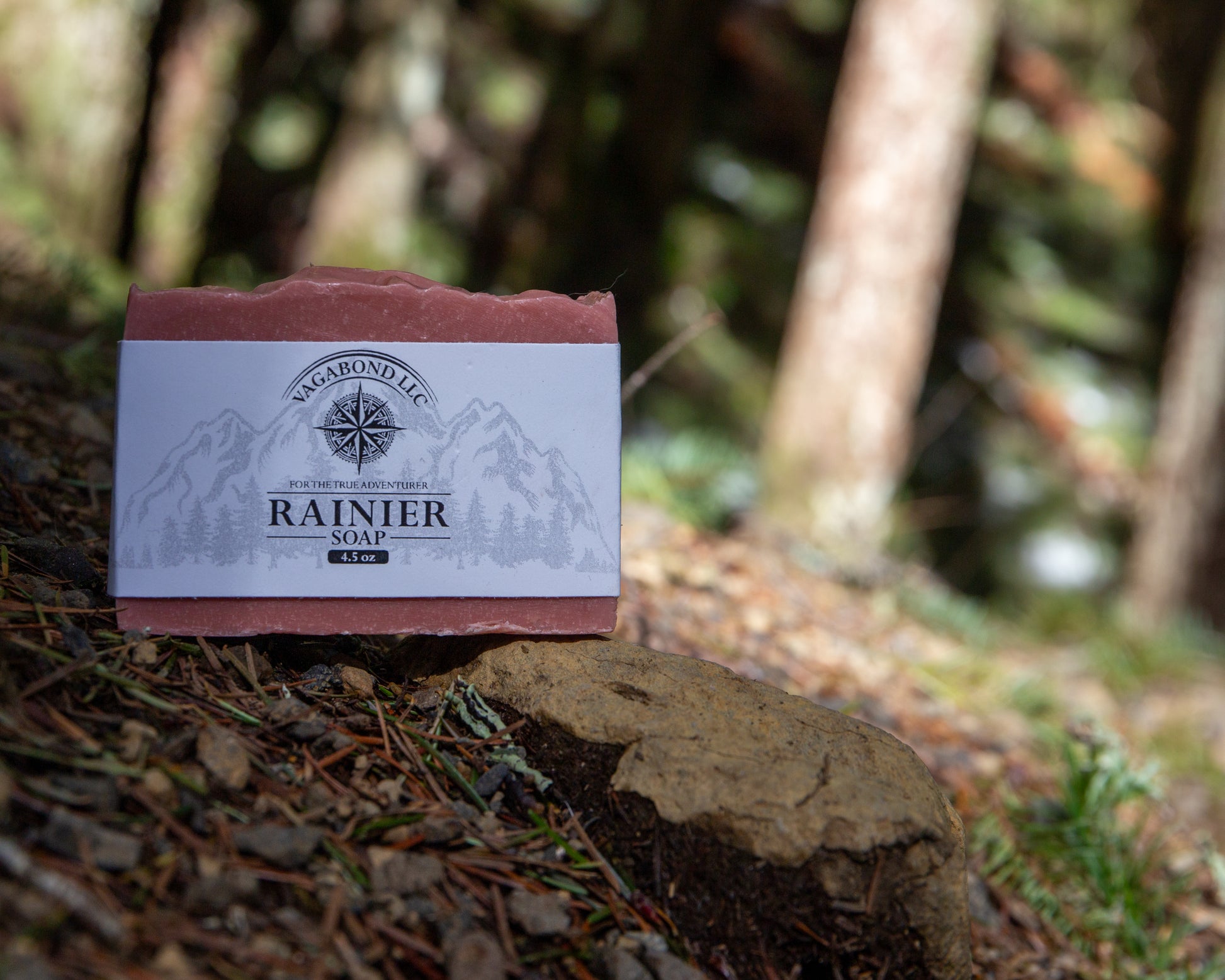 Rainier natural bar soap warm cinnamon scent on a log displayed with climbing gear against a forest backdrop.