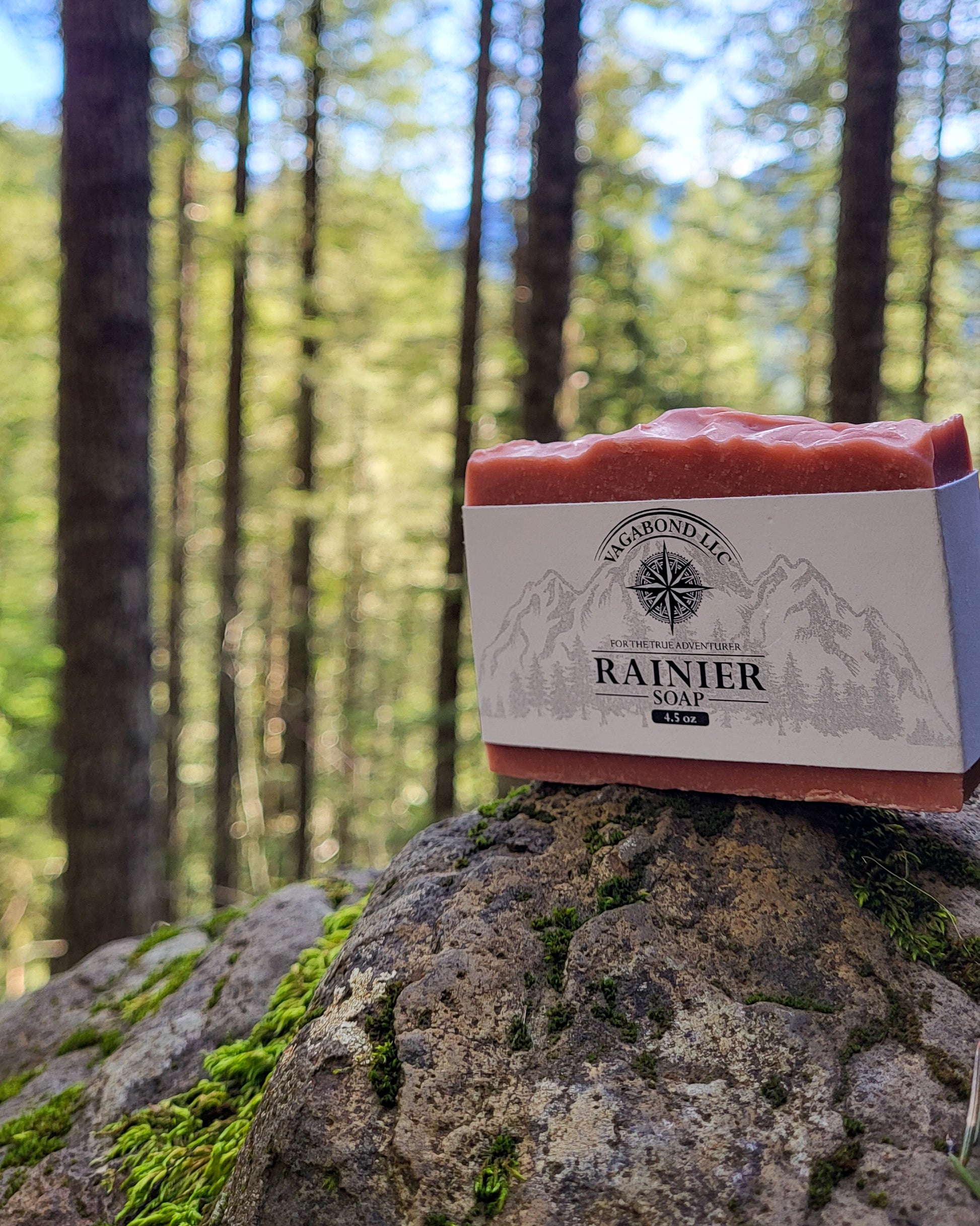 Rainier natural bar soap warm cinnamon scent on a log displayed with climbing gear against a woods backdrop.