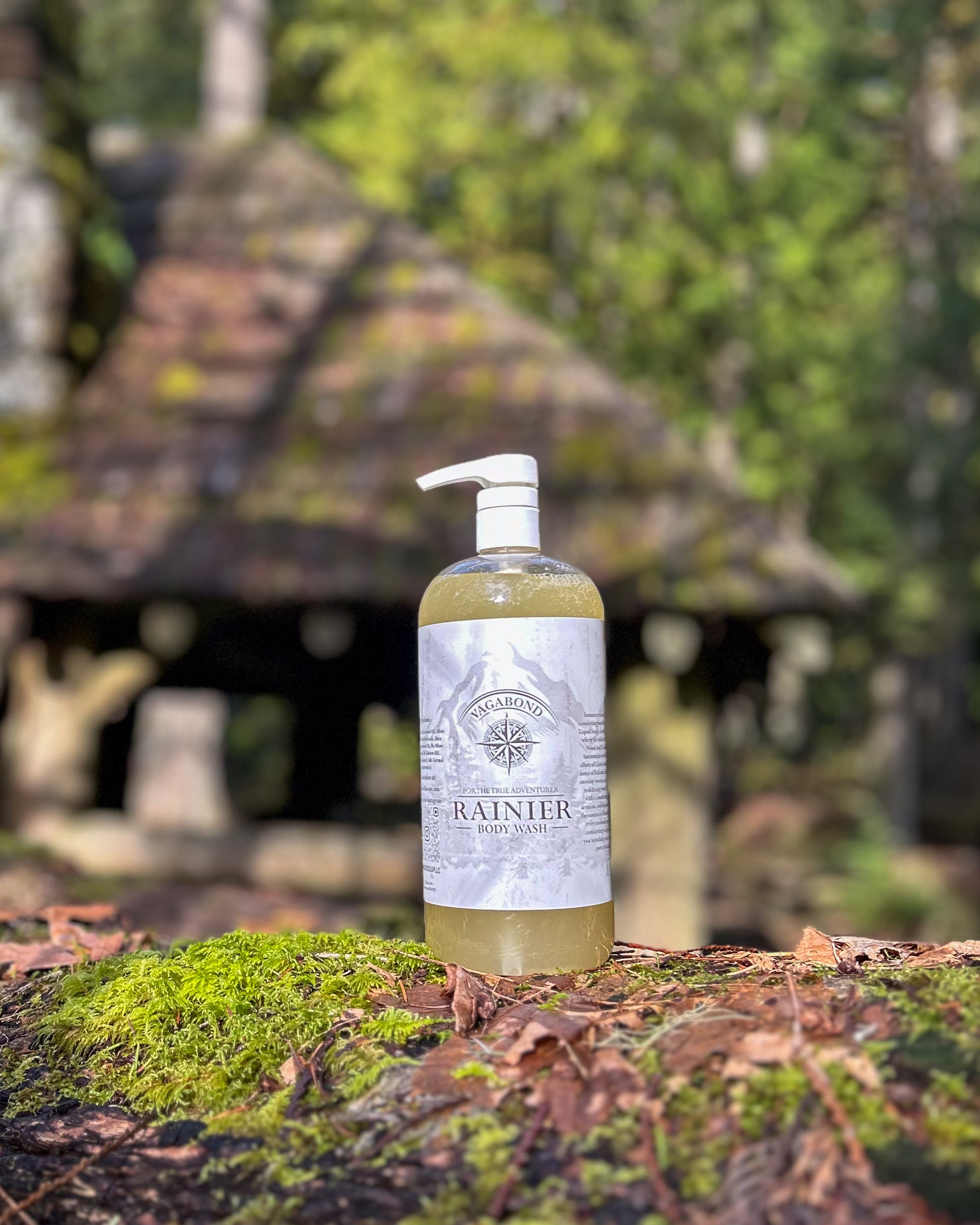 Rainier natural body wash warm cinnamon scent displayed against a mossy cabin backdrop