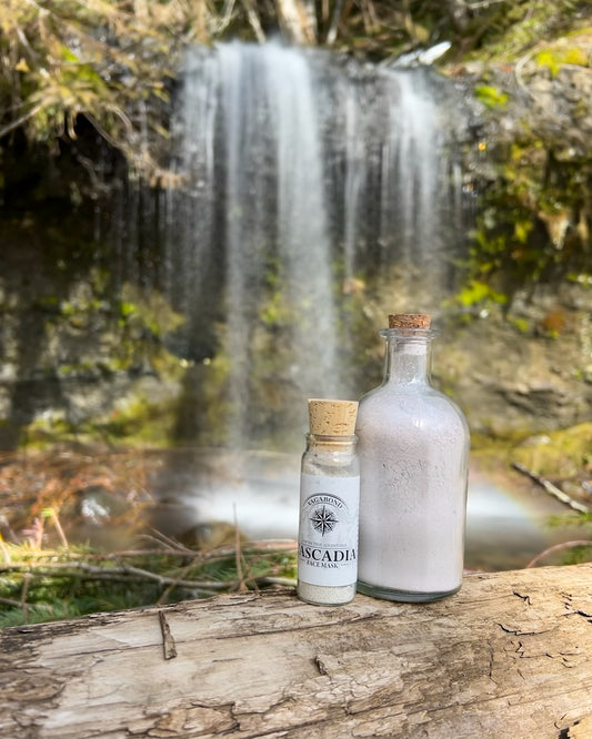 Cascadia natural clay mask in corked glass bottles displayed against a serene waterfall backdrop.