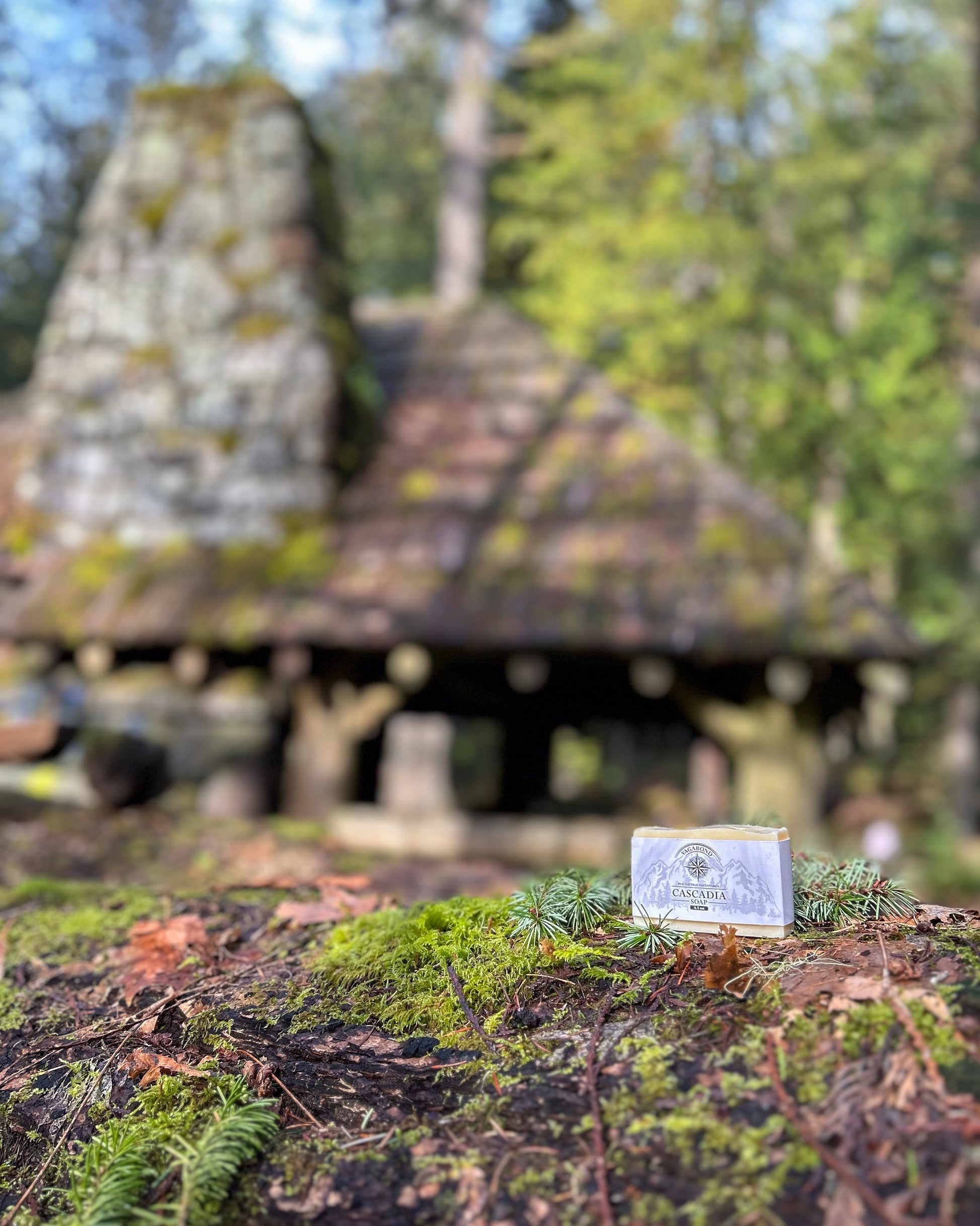 Cascadia natural bar soap lemon citrus scent on a moss covered rock displayed against a blurry cabin backdrop.