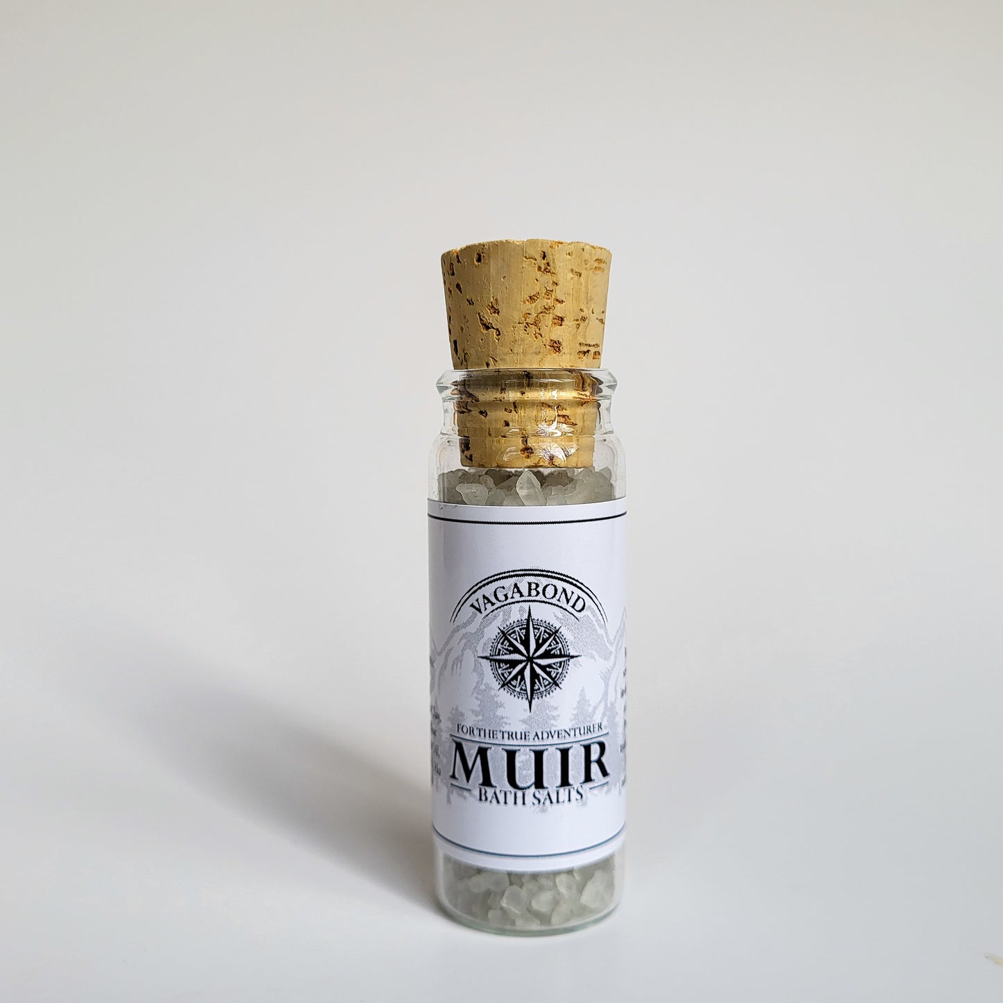 Muir natural bath salts evergreen scent in corked glass bottle displayed against a white backdrop showing logo on label