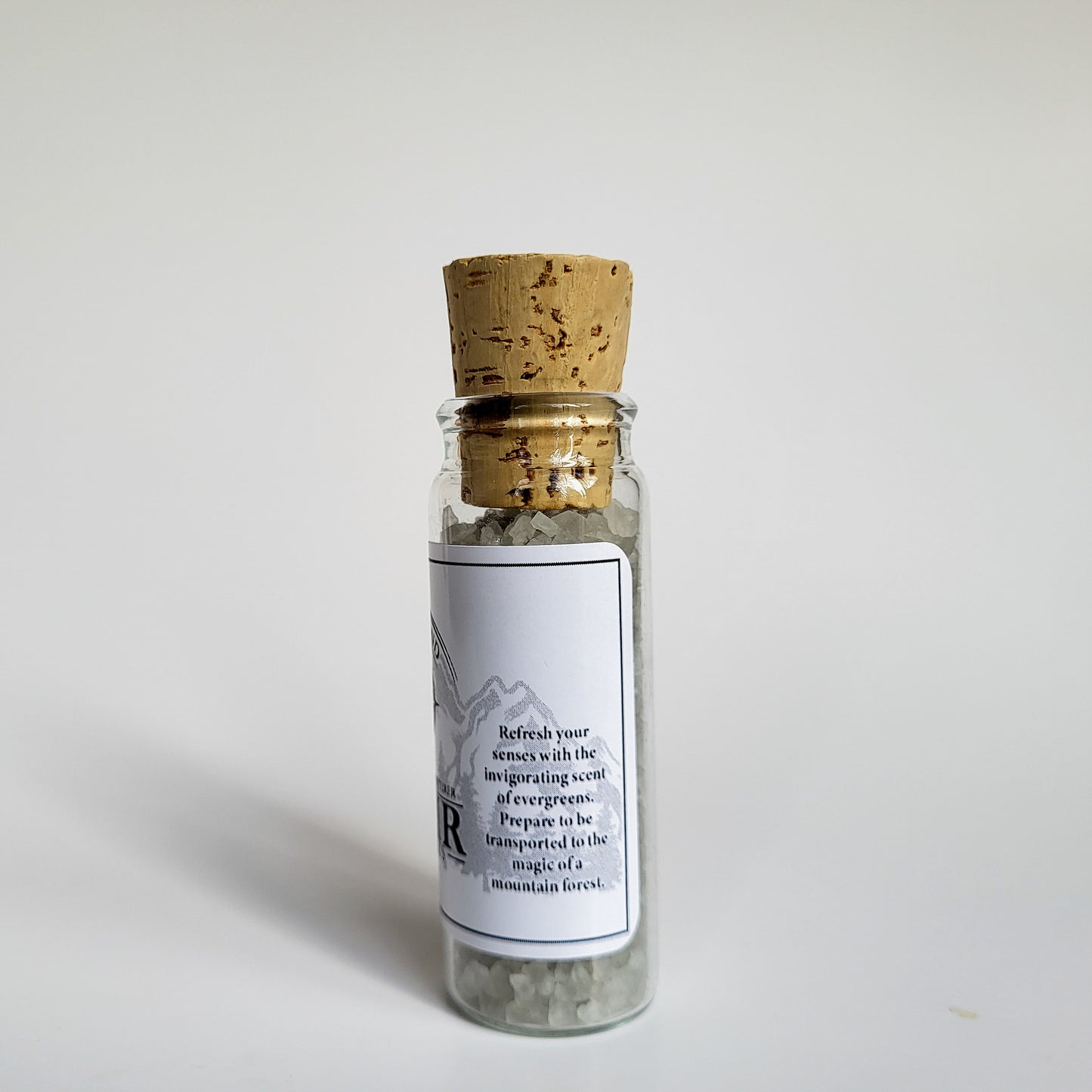 Muir natural bath salts evergreen scent in corked glass bottle displayed against a white backdrop showing description on label