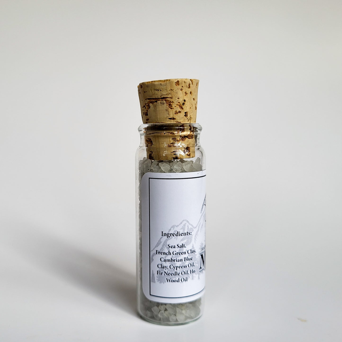 Muir natural bath salts evergreen scent in corked glass bottle displayed against a white backdrop showing ingredients on label