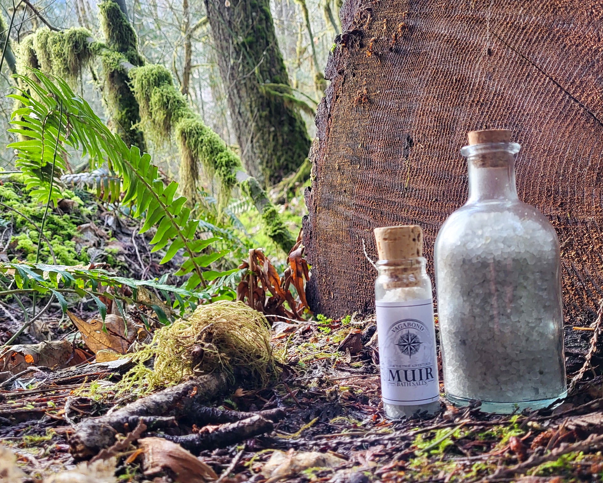 Muir natural bath salts evergreen scent in corked glass bottles displayed on a split log backdrop