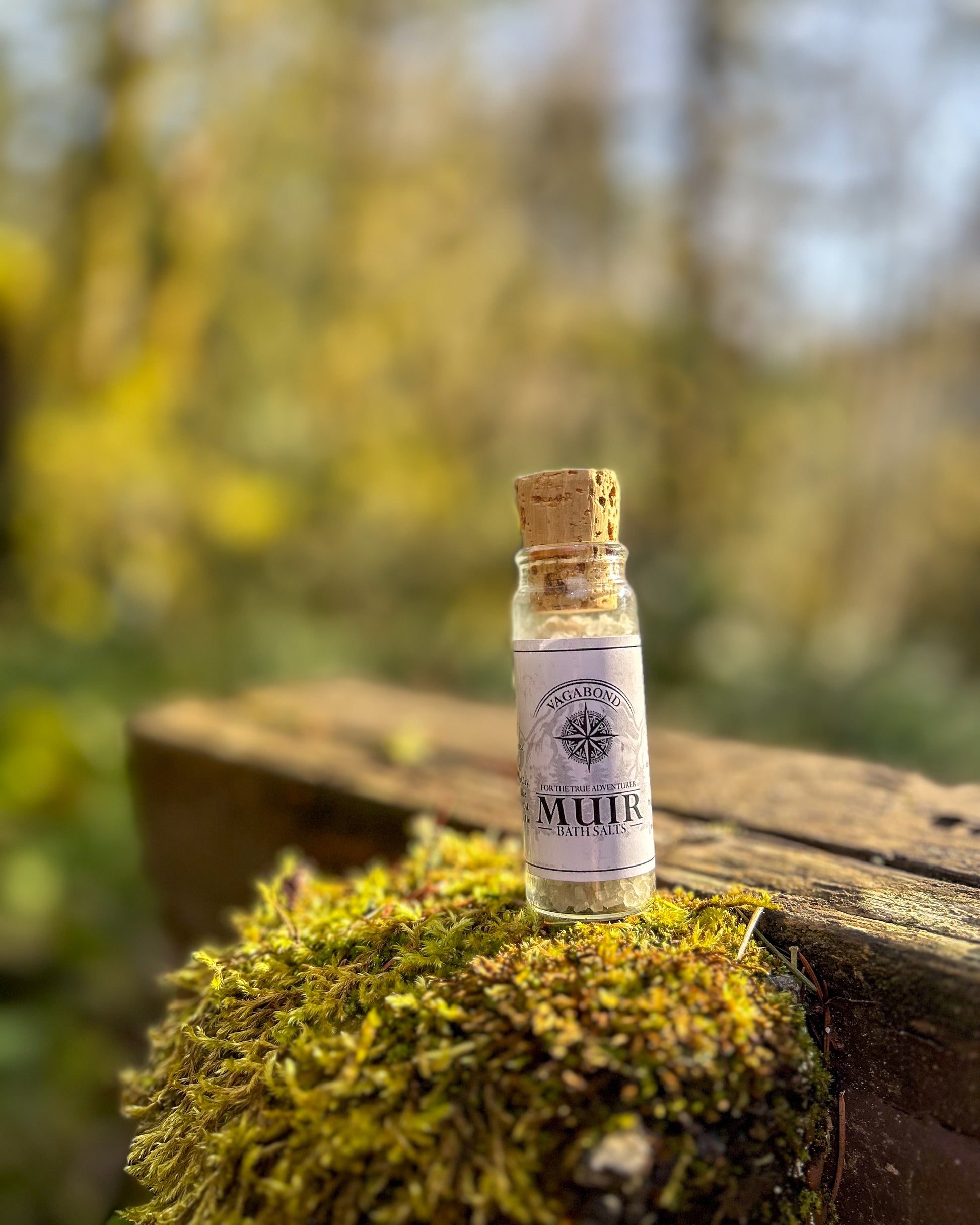 Muir natural bath salts evergreen scent in corked glass bottles displayed on a mossy stump backdrop