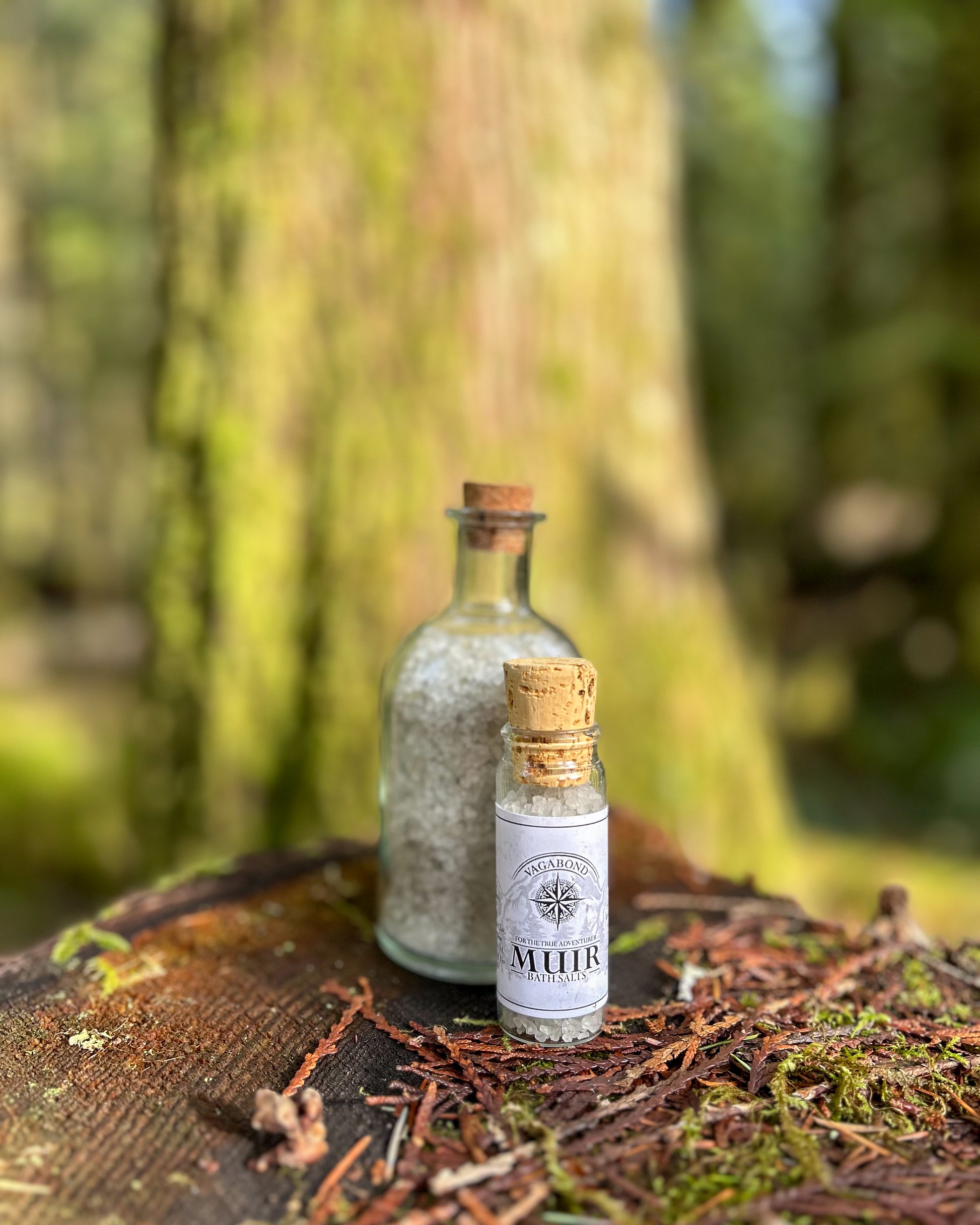 Muir natural bath salts evergreen scent in corked glass bottles displayed on a cut stump backdrop