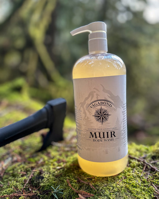 Muir natural body wash evergreen scent in corked glass bottles displayed on a mossy log with an axe backdrop