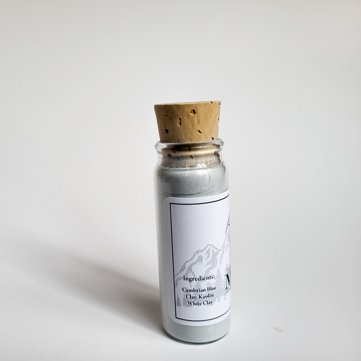 Muir natural clay mask in corked glass bottle displayed against a plain white backdrop showing ingredients on the label