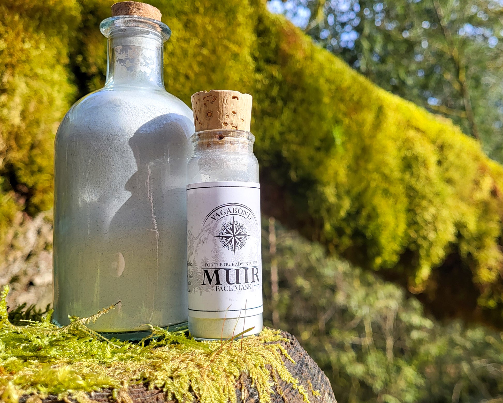 Muir natural clay mask in corked glass bottles displayed on a mossy stump backdrop.