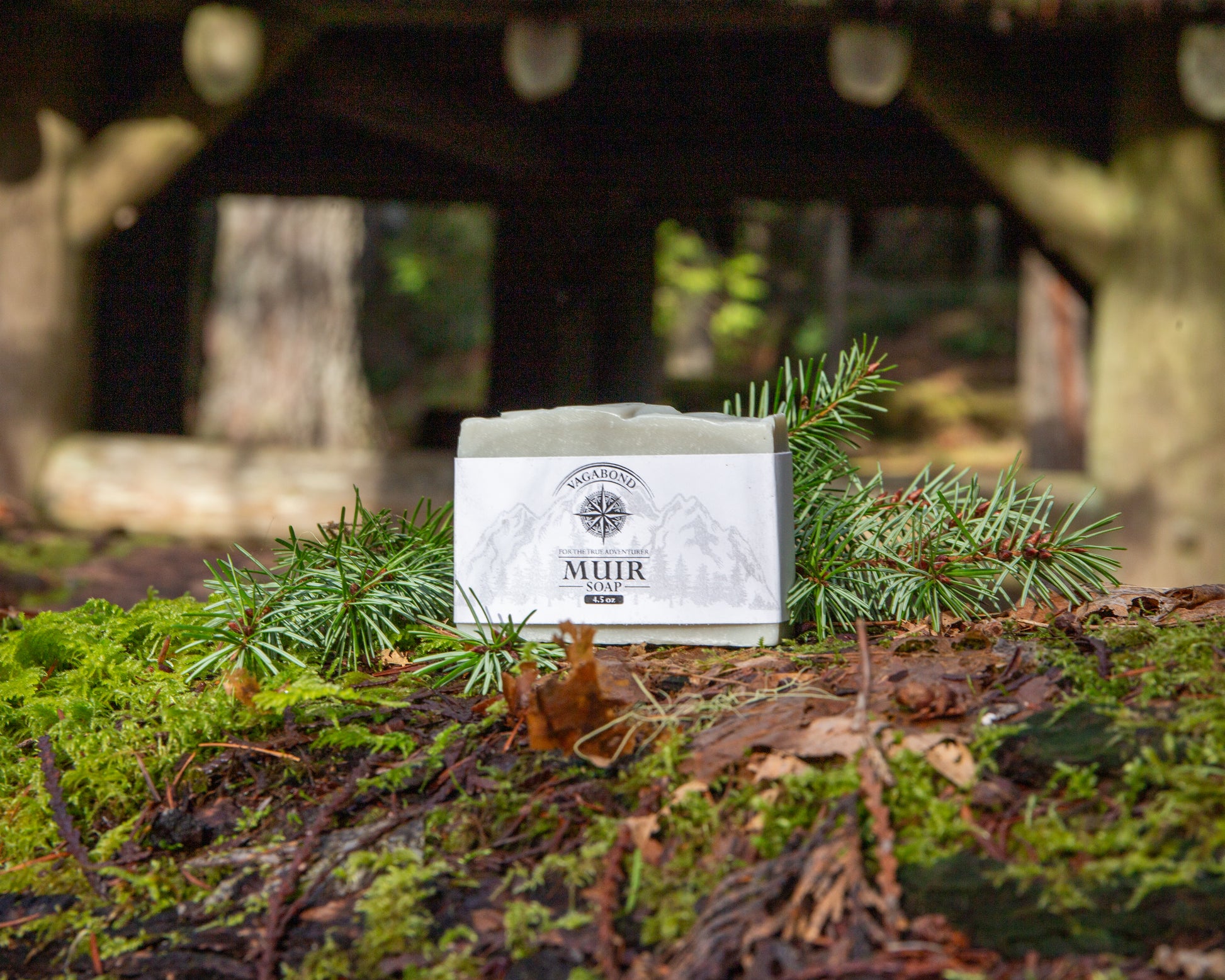 Muir natural bar soap evergreen scent displayed on a mossy log with cabin backdrop