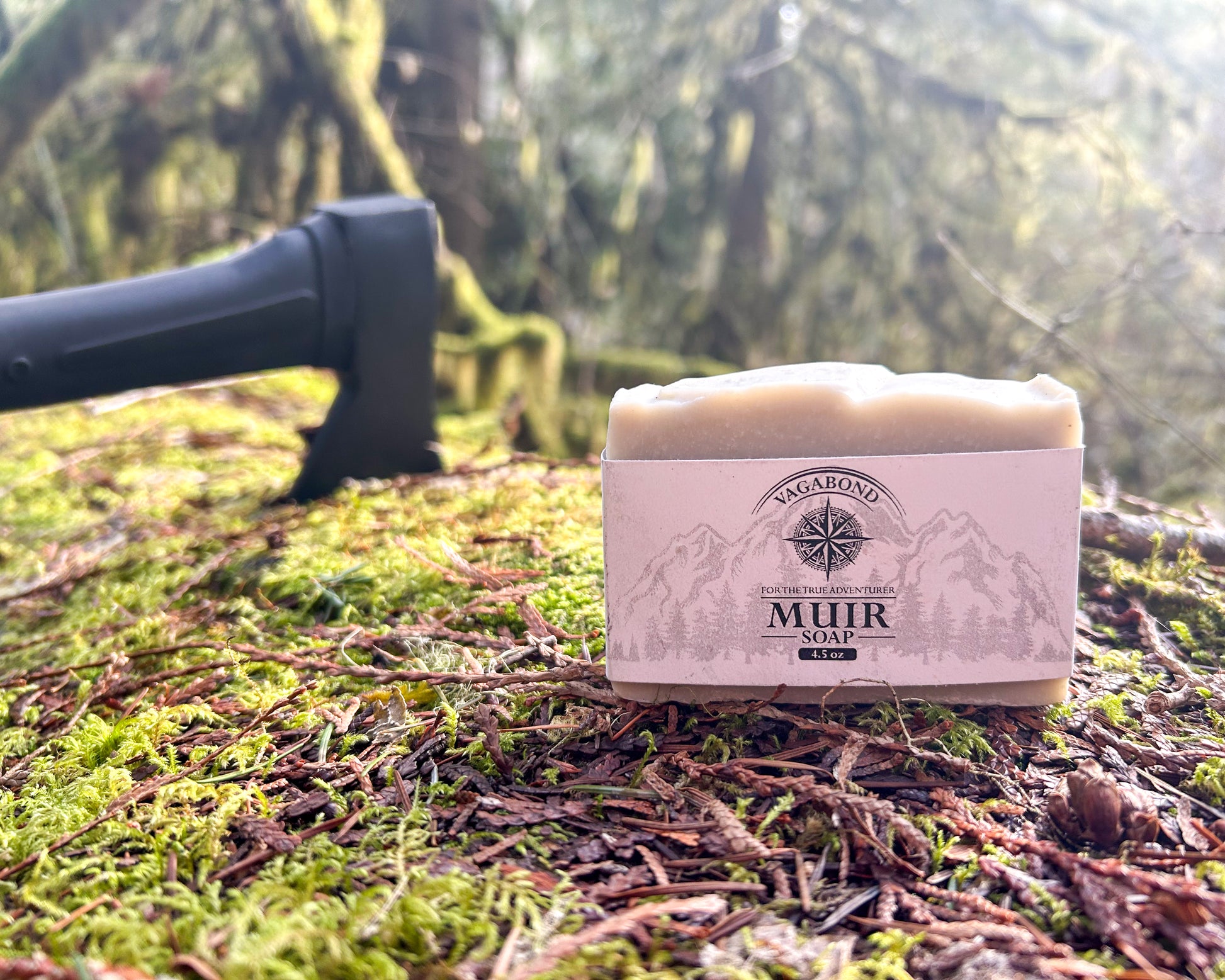 Muir natural bar soap evergreen scent displayed on a mossy log with axe backdrop