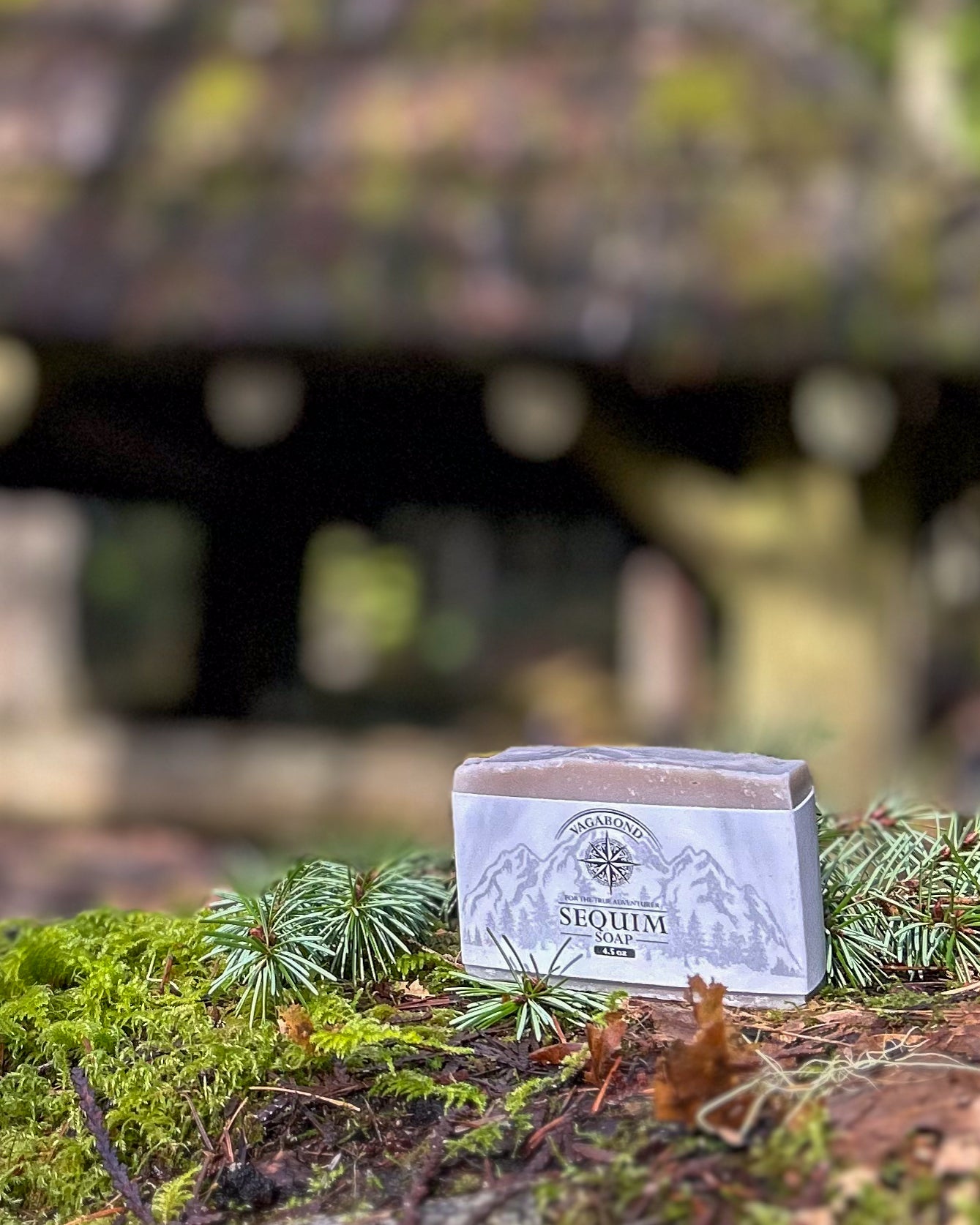 Sequim natural bar soap lavender mint scent on a mossy stump displayed against a blurry cabin backdrop.