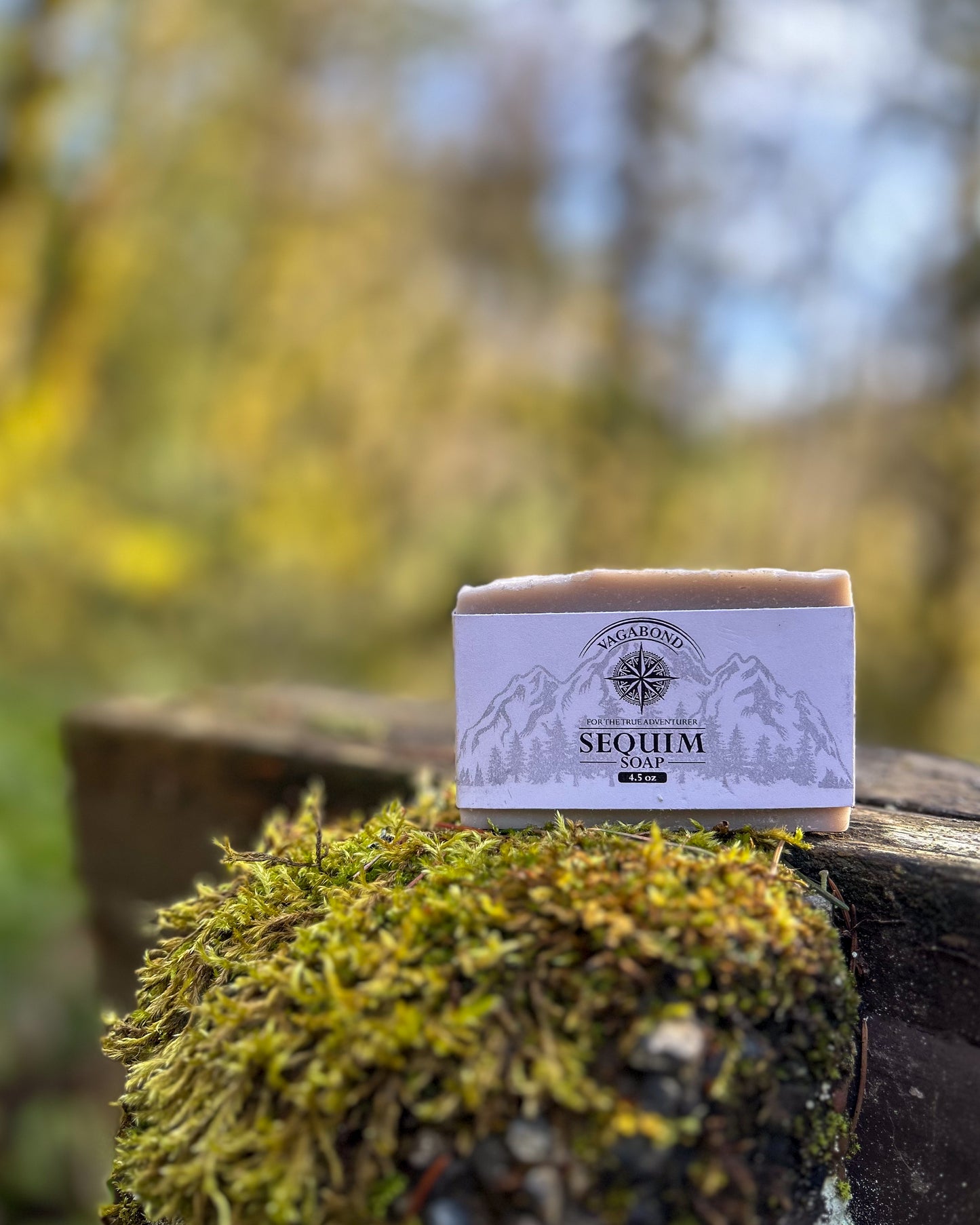 Sequim natural bar soap lavender mint scent on a mossy stump displayed against a blurry forest backdrop.